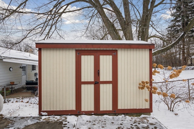 snow covered structure featuring a shed, an outdoor structure, and fence