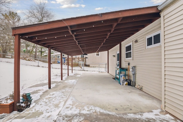 snow covered patio featuring fence and an attached carport