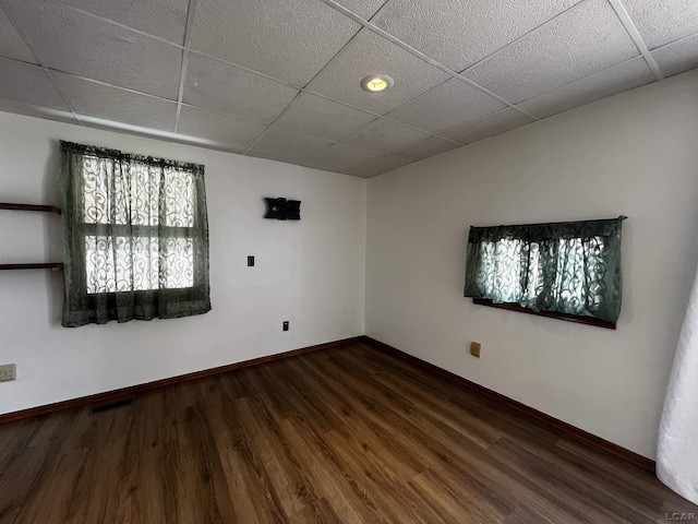 empty room with a drop ceiling, baseboards, and wood finished floors