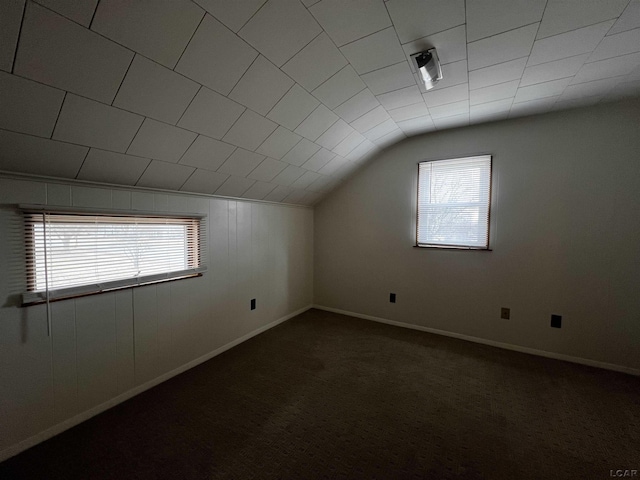 additional living space with vaulted ceiling, dark carpet, and baseboards