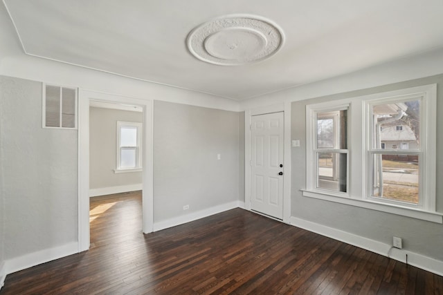 unfurnished room featuring dark wood-type flooring, visible vents, and baseboards