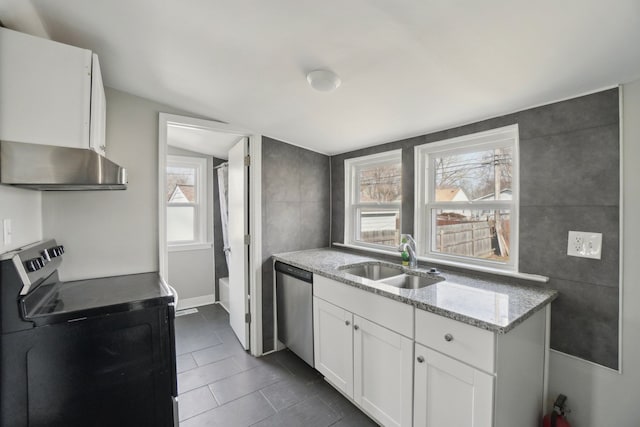 kitchen with white cabinets, dark tile patterned flooring, appliances with stainless steel finishes, light stone countertops, and a sink