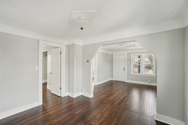 unfurnished room with arched walkways, wood-type flooring, and baseboards