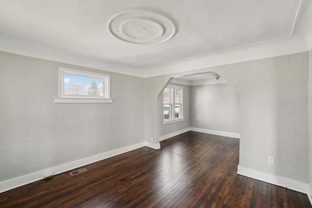 empty room with arched walkways, hardwood / wood-style floors, visible vents, and baseboards