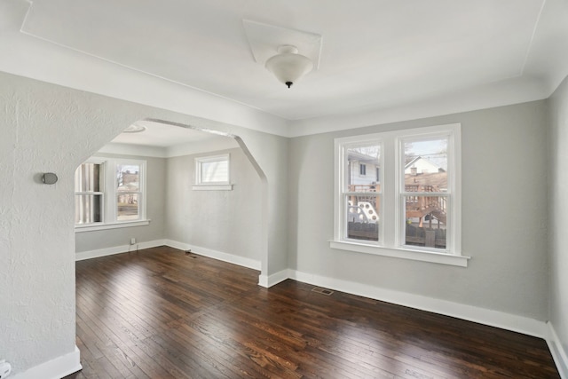 empty room featuring arched walkways, baseboards, and hardwood / wood-style floors