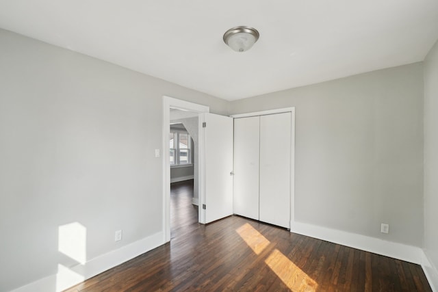 unfurnished bedroom featuring dark wood-style floors, a closet, and baseboards