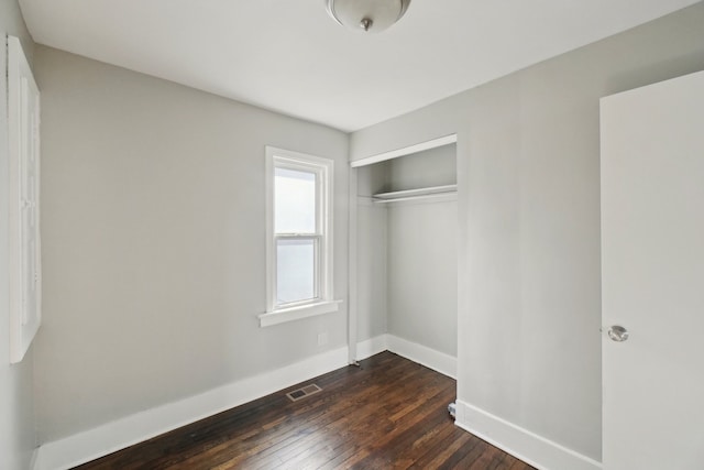 unfurnished bedroom with dark wood-type flooring, a closet, visible vents, and baseboards