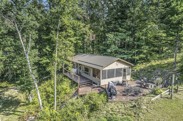 exterior space featuring a forest view, a sunroom, metal roof, and a wooden deck