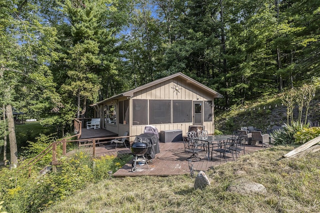 rear view of house featuring outdoor dining space, a sunroom, and a wooden deck