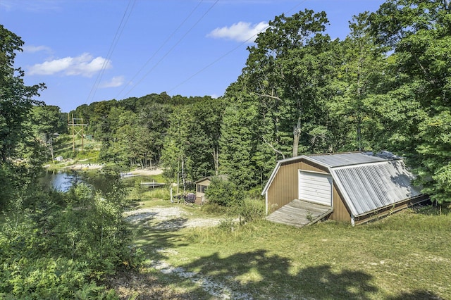 view of yard with a garage, driveway, an outbuilding, and a view of trees