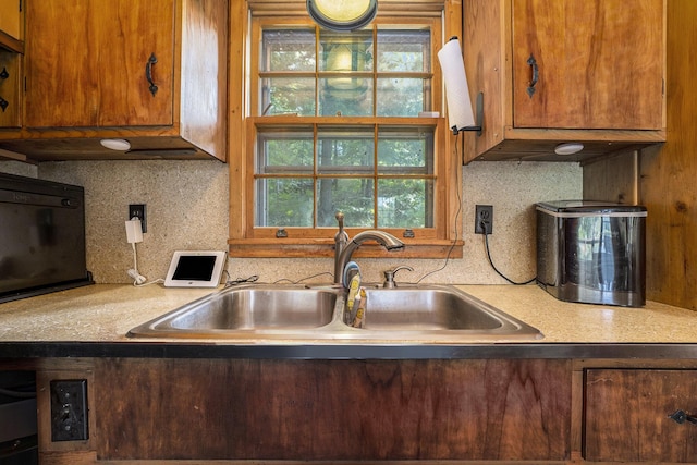 kitchen featuring brown cabinets, backsplash, a sink, and light countertops