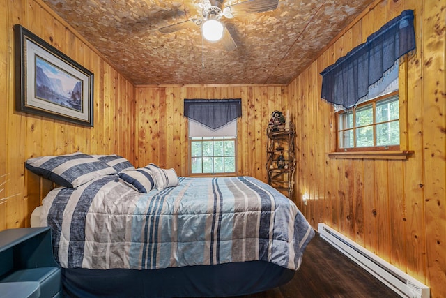 bedroom with a baseboard heating unit, wood walls, multiple windows, and a ceiling fan