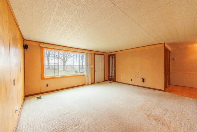 spare room with visible vents, baseboards, an ornate ceiling, carpet floors, and wood walls