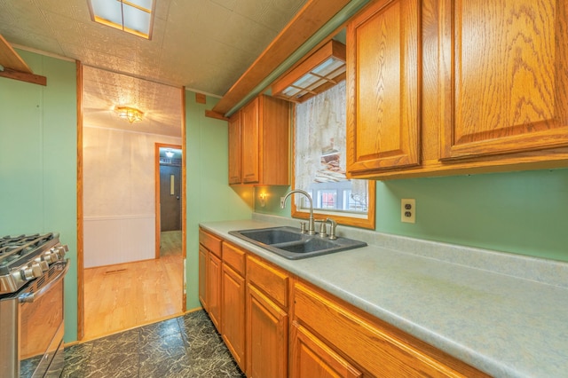 kitchen featuring stainless steel gas range, light countertops, brown cabinetry, and a sink