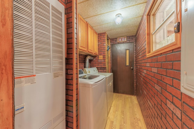 laundry area featuring washing machine and clothes dryer, cabinet space, light wood-style floors, a heating unit, and brick wall