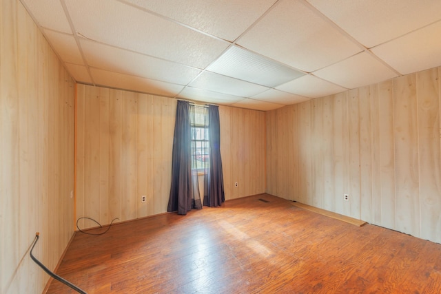 empty room featuring light wood-style floors, a drop ceiling, and wooden walls