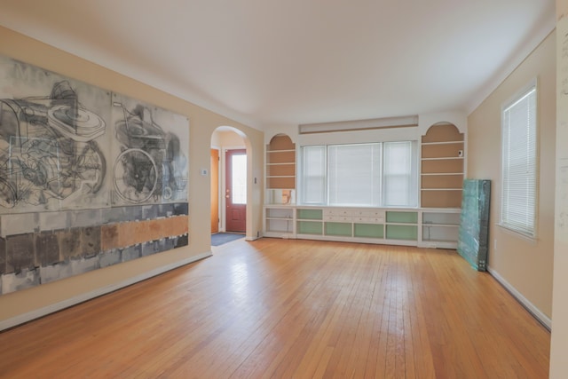 unfurnished room featuring hardwood / wood-style flooring, baseboards, and arched walkways