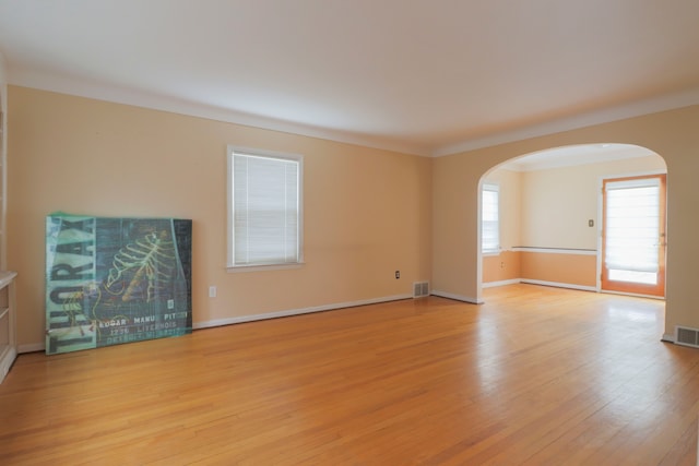 unfurnished living room featuring arched walkways, visible vents, baseboards, and wood finished floors