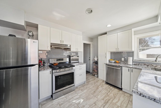 kitchen with appliances with stainless steel finishes, white cabinets, a sink, light stone countertops, and under cabinet range hood