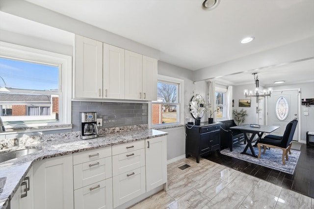 kitchen featuring light stone counters, backsplash, a sink, and white cabinetry