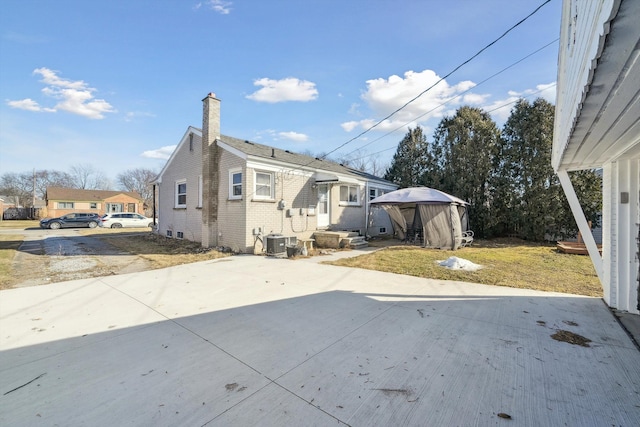 back of house featuring a chimney, a patio area, cooling unit, and a lawn