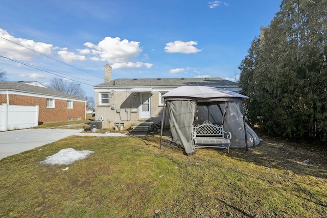 back of property with brick siding, a chimney, a lawn, central AC unit, and entry steps