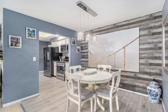 dining area featuring light wood-style flooring, wooden walls, an accent wall, and baseboards