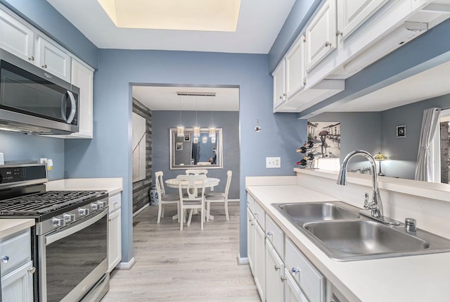 kitchen featuring white cabinets, stainless steel appliances, light countertops, light wood-type flooring, and a sink