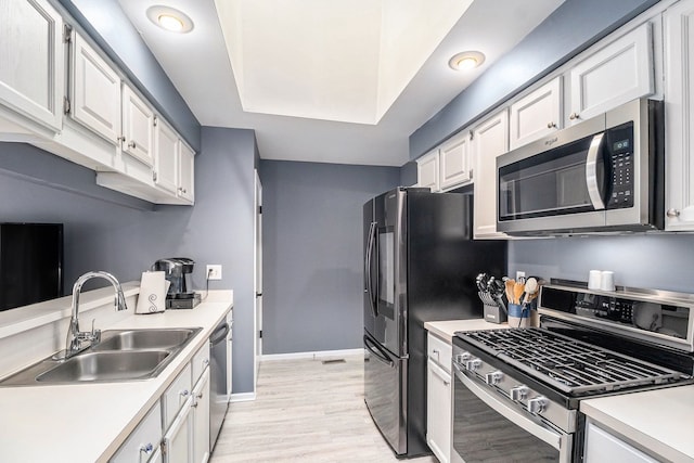 kitchen with stainless steel appliances, a sink, light countertops, and white cabinets