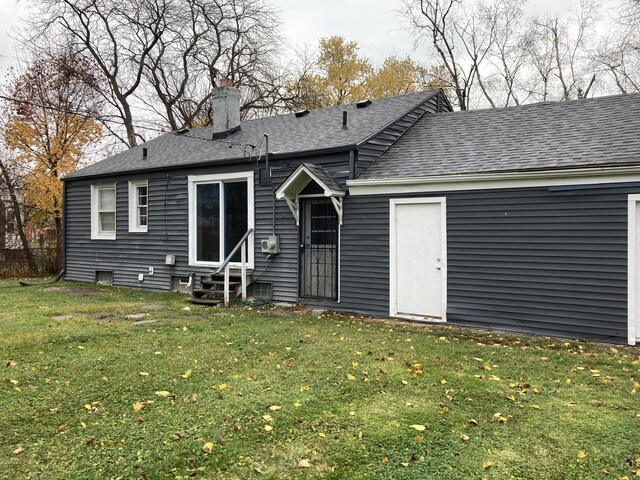 back of house with entry steps, a shingled roof, a lawn, and a chimney