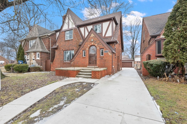 tudor house with a shingled roof, stucco siding, a detached garage, an outbuilding, and brick siding