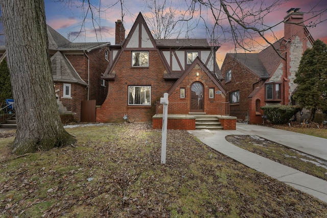 tudor home featuring stucco siding, roof with shingles, a chimney, and brick siding