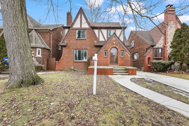 tudor home with brick siding, a chimney, a shingled roof, and stucco siding