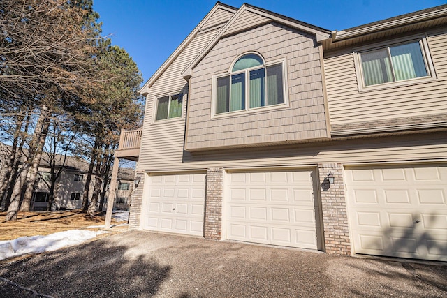 view of front facade featuring brick siding, an attached garage, a balcony, and aphalt driveway