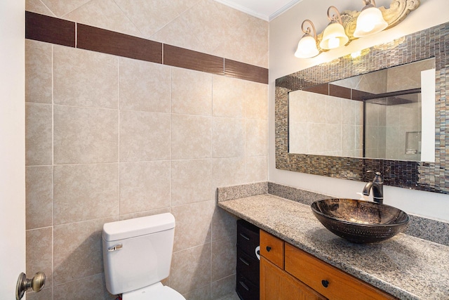 bathroom with tile walls, toilet, ornamental molding, vanity, and tiled shower