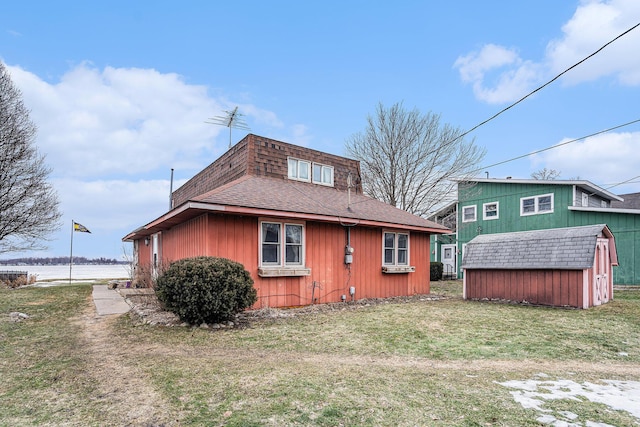 back of property featuring a yard, a storage unit, an outbuilding, and roof with shingles