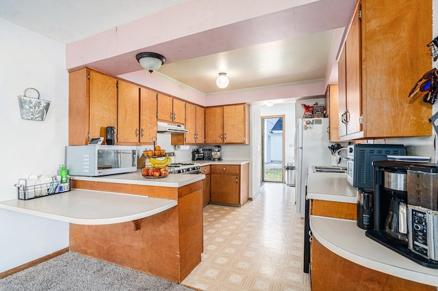 kitchen with white microwave, under cabinet range hood, a peninsula, light floors, and brown cabinetry