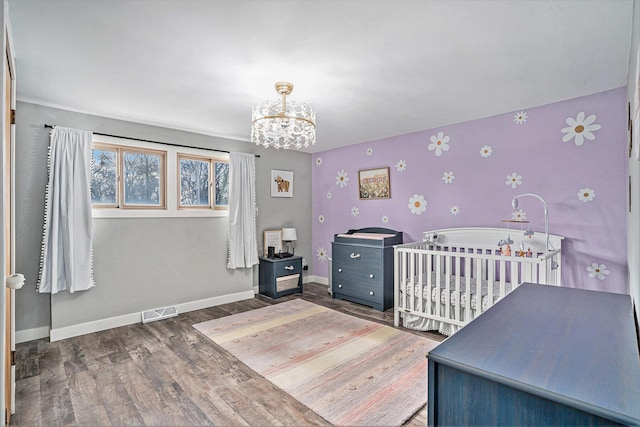 bedroom with visible vents, a notable chandelier, baseboards, and wood finished floors