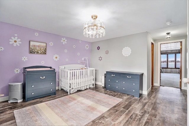 bedroom with an inviting chandelier, a crib, baseboards, and wood finished floors