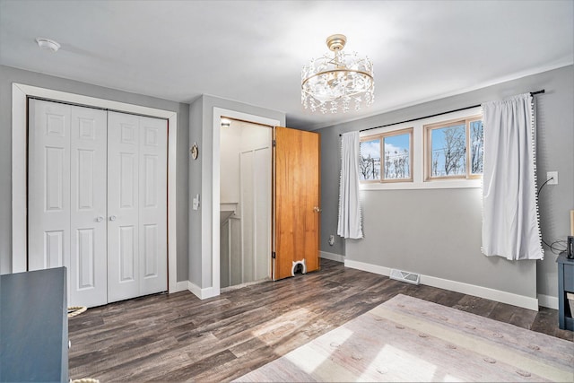 unfurnished bedroom with baseboards, visible vents, wood finished floors, a chandelier, and a closet