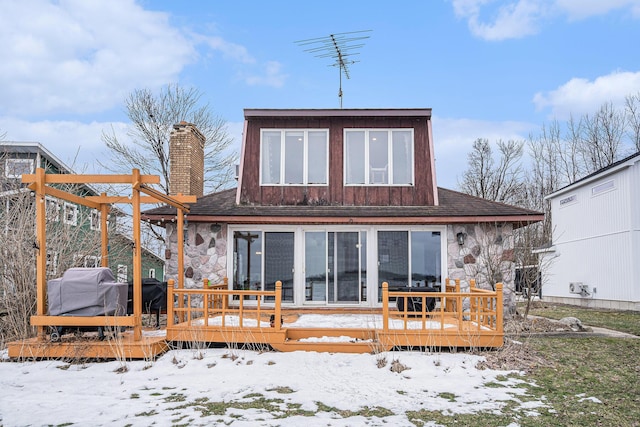 snow covered back of property featuring stone siding, a chimney, and a wooden deck