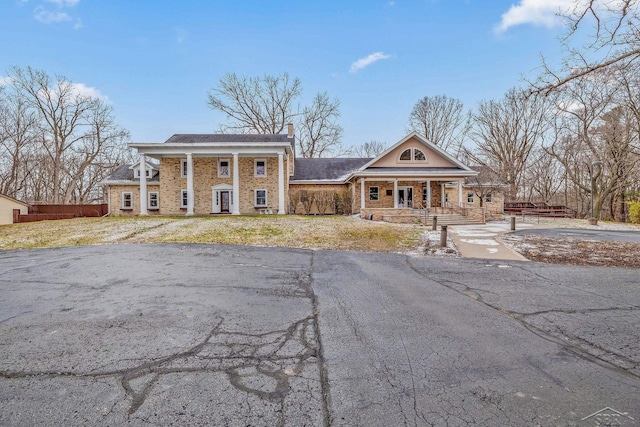 greek revival house with stone siding, a porch, a chimney, and fence