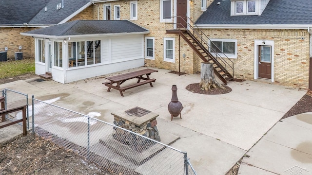 rear view of house with a shingled roof, a patio, a sunroom, stairway, and brick siding