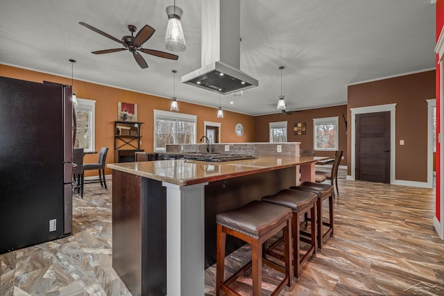 kitchen featuring island exhaust hood, a breakfast bar area, a ceiling fan, freestanding refrigerator, and light stone countertops