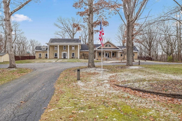 neoclassical home with aphalt driveway, stone siding, fence, and a chimney