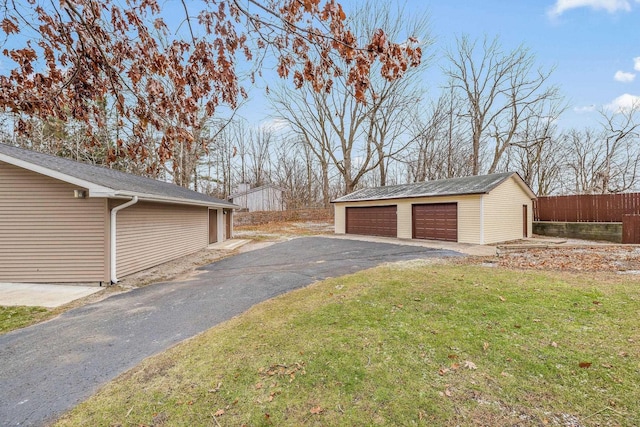 view of side of property with a lawn, fence, a detached garage, and an outbuilding