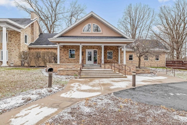 greek revival inspired property with covered porch, brick siding, a chimney, and a shingled roof