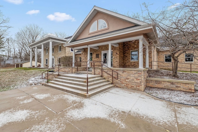 greek revival inspired property featuring covered porch, brick siding, and stucco siding