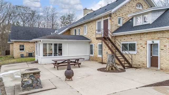 back of house with brick siding, a chimney, a shingled roof, stairway, and a patio area