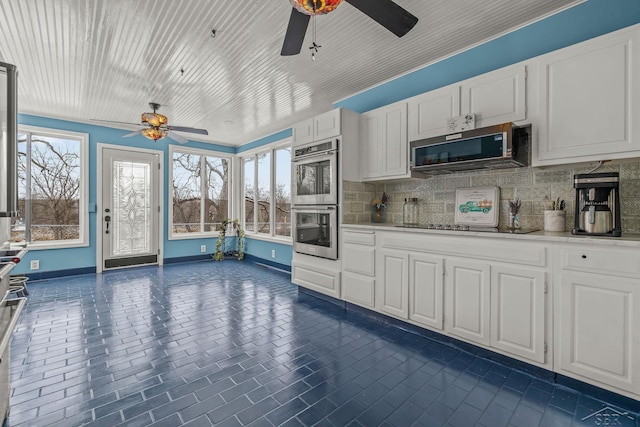 kitchen featuring white cabinetry, decorative backsplash, stainless steel appliances, baseboards, and a ceiling fan